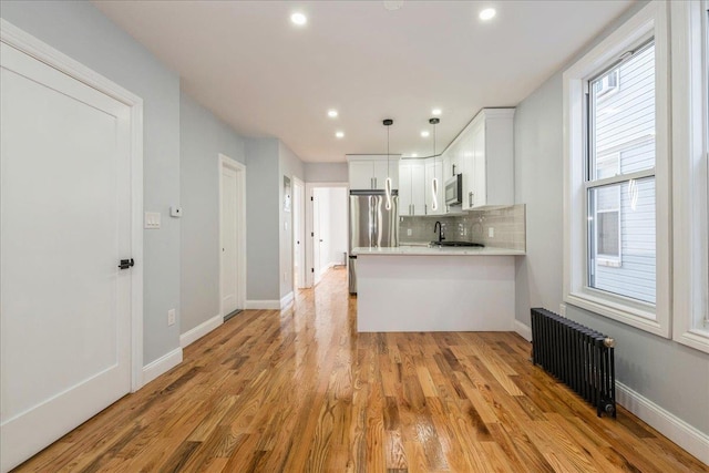 kitchen featuring radiator heating unit, appliances with stainless steel finishes, hanging light fixtures, white cabinets, and kitchen peninsula