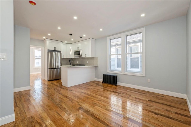 kitchen featuring appliances with stainless steel finishes, radiator heating unit, decorative light fixtures, white cabinetry, and kitchen peninsula