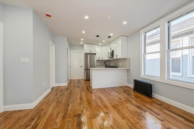 kitchen with kitchen peninsula, radiator heating unit, pendant lighting, appliances with stainless steel finishes, and white cabinets