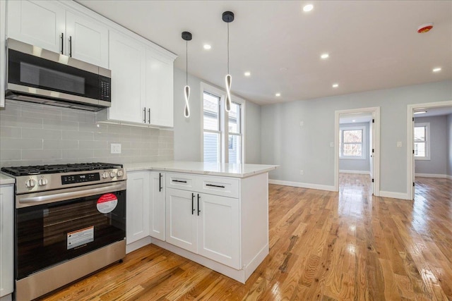 kitchen with white cabinets, decorative light fixtures, kitchen peninsula, and appliances with stainless steel finishes