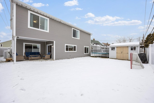 snow covered back of property featuring a shed, cooling unit, a hot tub, and a trampoline