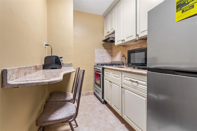 83-15 98th St Unit 6B, Woodhaven, NY 11421 - kitchen with stainless steel appliances, tasteful backsplash, under cabinet range hood, white cabinets, and a breakfast bar