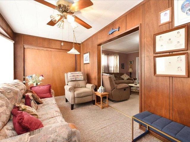 living room featuring wooden walls, light colored carpet, ceiling fan, and ornamental molding