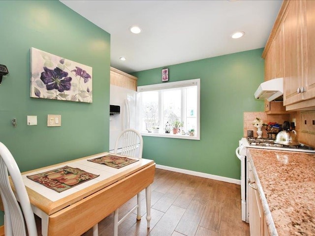 kitchen featuring light brown cabinetry, light hardwood / wood-style floors, extractor fan, tasteful backsplash, and white range with gas cooktop