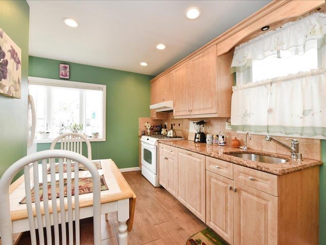 kitchen with light brown cabinetry, sink, light stone countertops, white gas stove, and light hardwood / wood-style floors