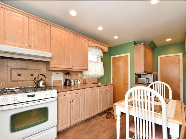 kitchen featuring light brown cabinetry, decorative backsplash, light wood-type flooring, dark stone countertops, and gas range gas stove