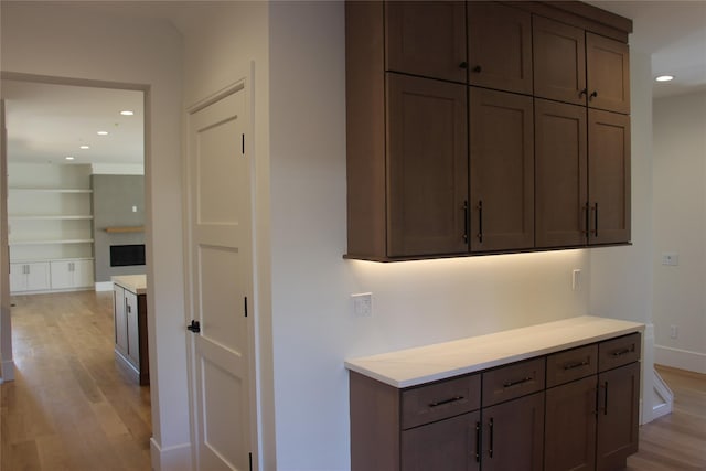 kitchen featuring built in features, dark brown cabinets, and light hardwood / wood-style flooring