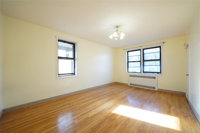 unfurnished room featuring radiator, a wealth of natural light, light hardwood / wood-style flooring, and a chandelier