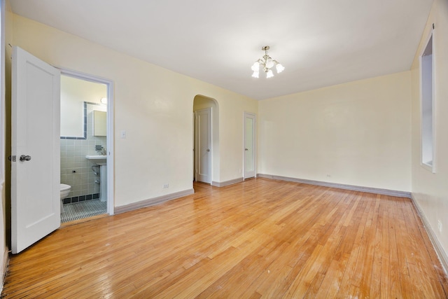 unfurnished bedroom with tile walls, light hardwood / wood-style floors, ensuite bathroom, and an inviting chandelier