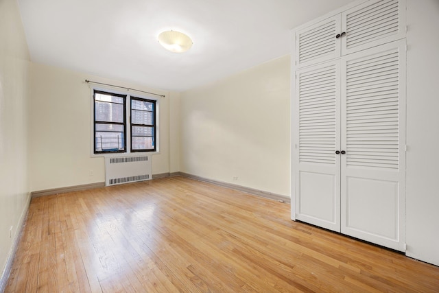 unfurnished bedroom featuring radiator, light hardwood / wood-style floors, and a closet