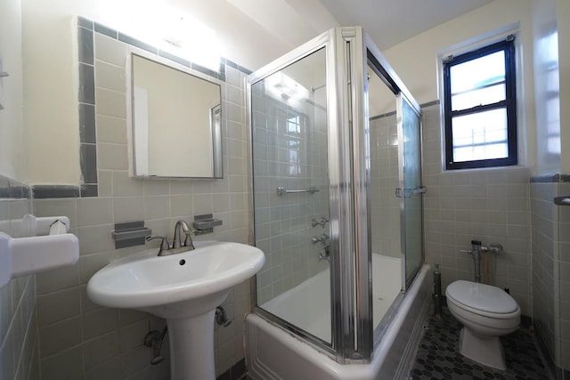 bathroom featuring toilet, tile patterned flooring, combined bath / shower with glass door, and tile walls