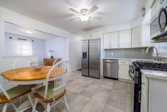 kitchen featuring ceiling fan, appliances with stainless steel finishes, backsplash, white cabinetry, and light tile patterned flooring