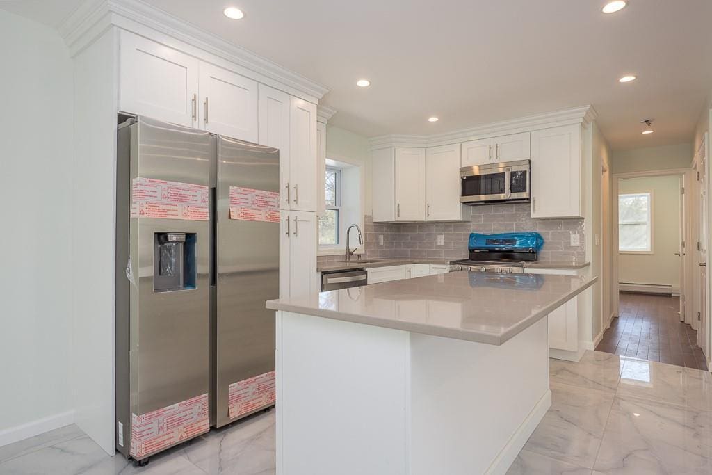 kitchen with sink, appliances with stainless steel finishes, backsplash, white cabinets, and a kitchen island