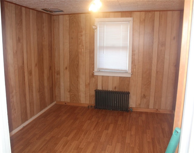 unfurnished room with hardwood / wood-style floors, radiator heating unit, and wooden walls