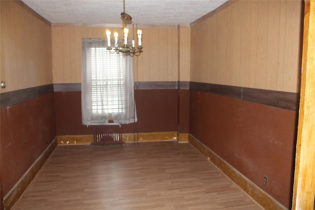 unfurnished dining area with a chandelier, radiator, and wood-type flooring