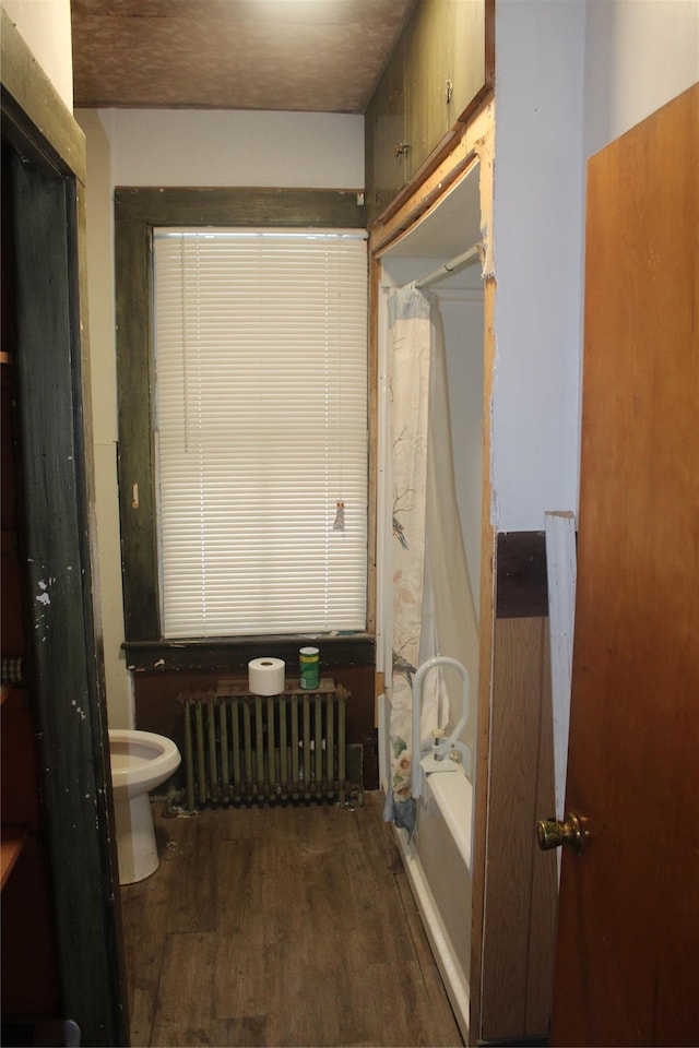 bathroom featuring wood-type flooring, radiator heating unit, toilet, and shower / bathtub combination with curtain