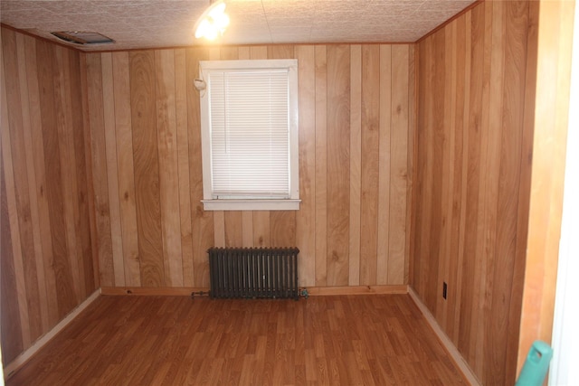 spare room featuring hardwood / wood-style flooring, radiator heating unit, and wooden walls