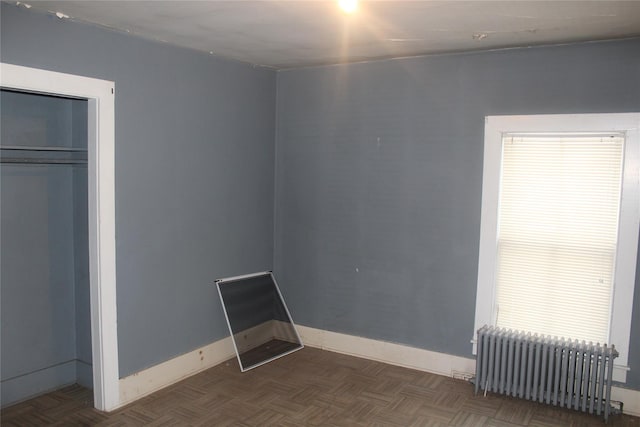 unfurnished bedroom with a closet, dark parquet floors, and radiator