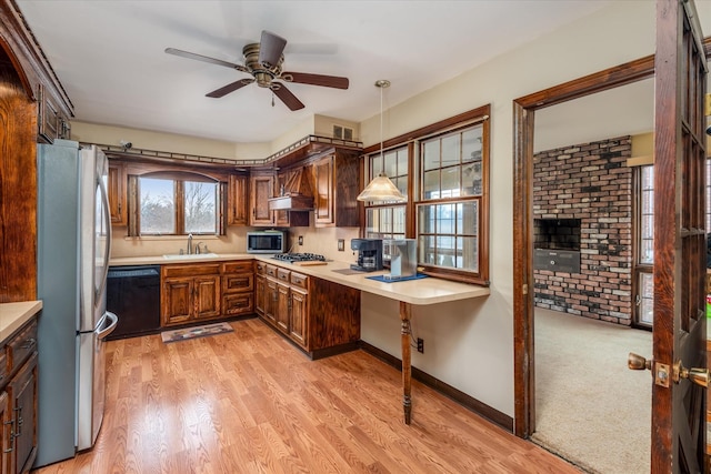 kitchen featuring decorative light fixtures, stainless steel appliances, sink, premium range hood, and light hardwood / wood-style flooring