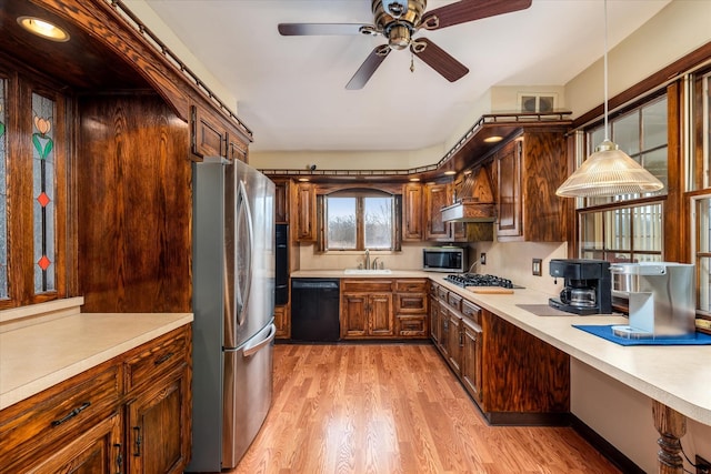 kitchen with decorative light fixtures, stainless steel appliances, sink, light wood-type flooring, and ceiling fan