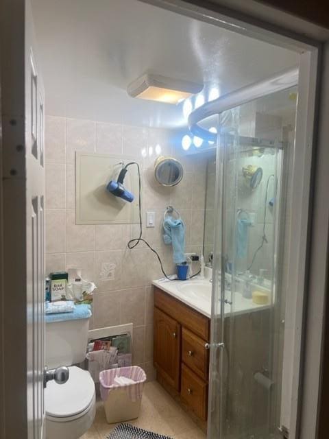 bathroom featuring tile patterned floors, a shower with door, vanity, tile walls, and toilet