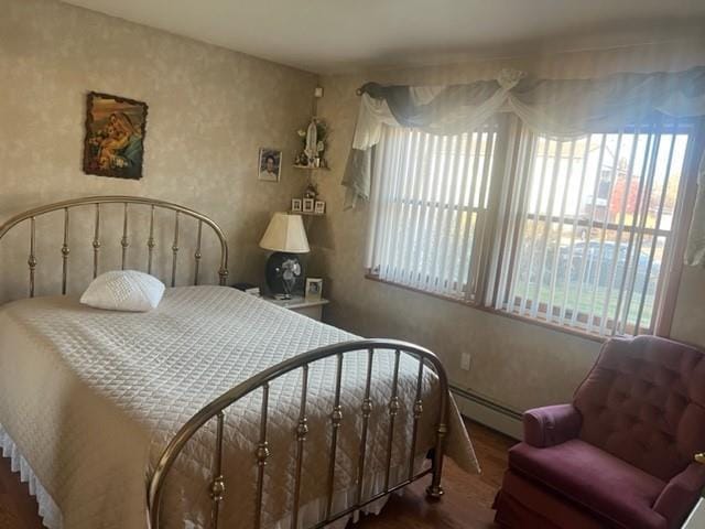 bedroom with hardwood / wood-style floors, multiple windows, and a baseboard heating unit