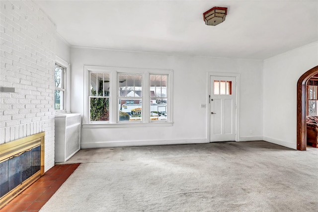 living room with a fireplace, dark colored carpet, crown molding, and a healthy amount of sunlight