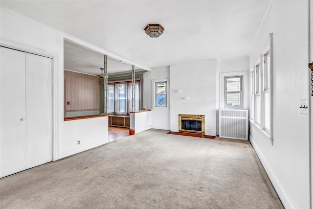 unfurnished living room with crown molding, carpet floors, radiator, and a brick fireplace