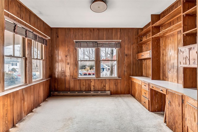 carpeted office space with baseboard heating, a wealth of natural light, wood walls, and built in desk