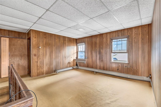 carpeted spare room featuring baseboard heating, a paneled ceiling, and wood walls