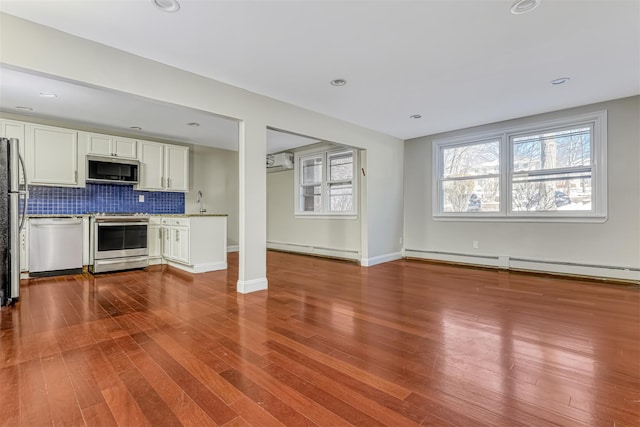 kitchen featuring a baseboard radiator, hardwood / wood-style floors, white cabinetry, stainless steel appliances, and backsplash