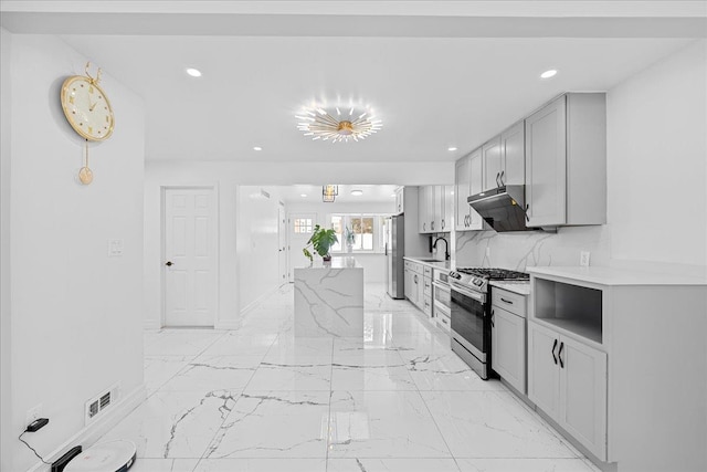 kitchen featuring sink, backsplash, gray cabinetry, light stone counters, and stainless steel gas range oven