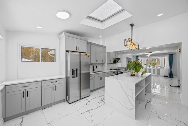 kitchen with light stone countertops, a kitchen island, stainless steel appliances, sink, and hanging light fixtures