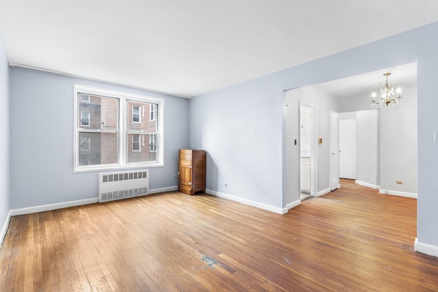 unfurnished room with wood-type flooring, radiator, and an inviting chandelier