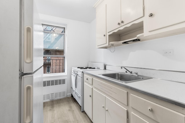 kitchen with white appliances, white cabinets, radiator heating unit, light hardwood / wood-style floors, and sink