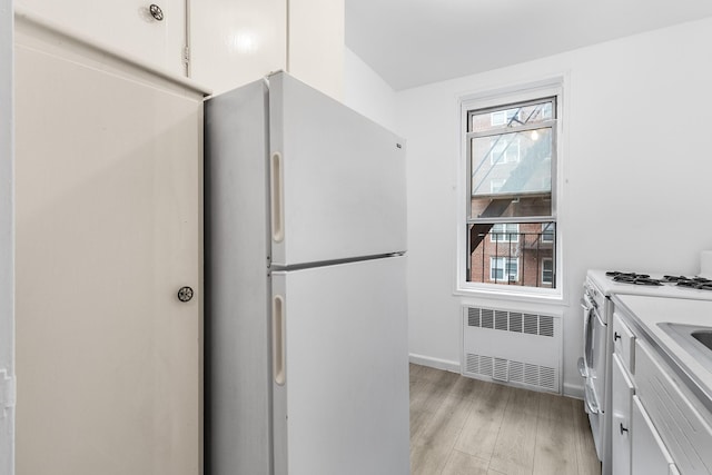 kitchen featuring light wood-type flooring, white cabinetry, white appliances, and radiator