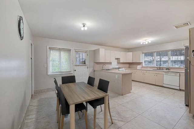 kitchen with sink, light tile patterned floors, white dishwasher, and kitchen peninsula