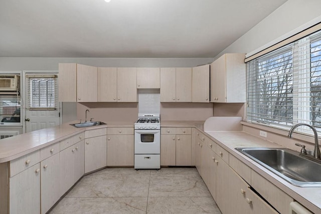 kitchen featuring cream cabinets, white range with gas cooktop, kitchen peninsula, and sink