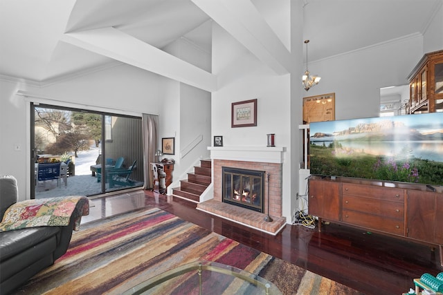 living room featuring dark wood-type flooring, a towering ceiling, an inviting chandelier, and a brick fireplace