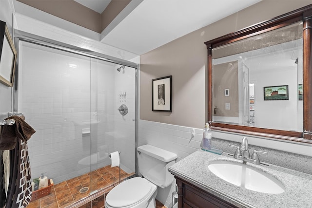 bathroom featuring vanity, toilet, a shower with shower door, and tile walls