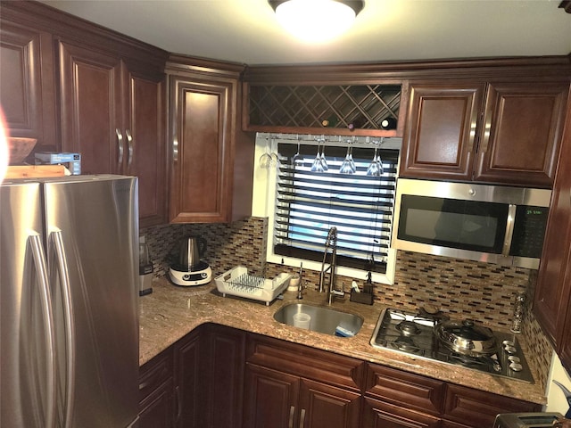 kitchen with dark brown cabinetry, stainless steel appliances, decorative backsplash, sink, and light stone counters