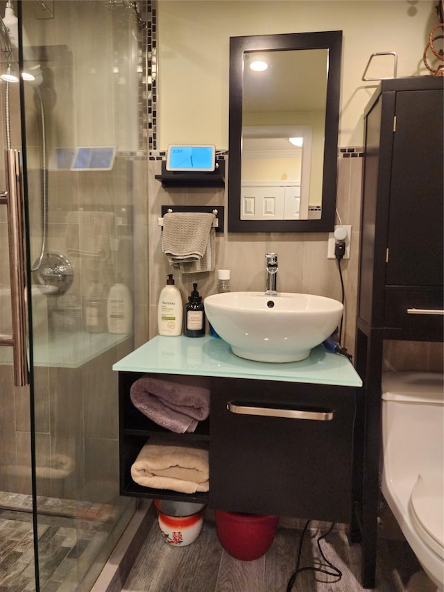 bathroom featuring toilet, hardwood / wood-style flooring, tile walls, vanity, and a shower with door