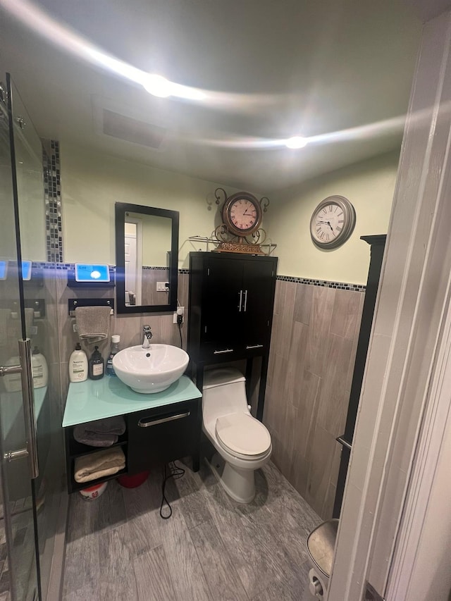 bathroom featuring tile walls, vanity, a shower with shower door, and toilet