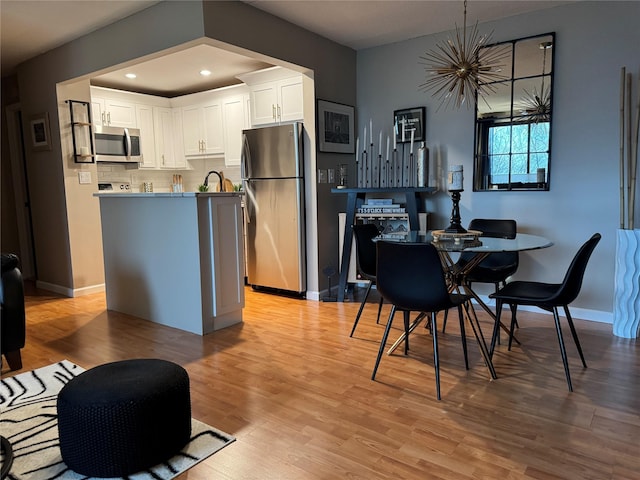 kitchen featuring appliances with stainless steel finishes, sink, white cabinets, decorative backsplash, and light hardwood / wood-style floors