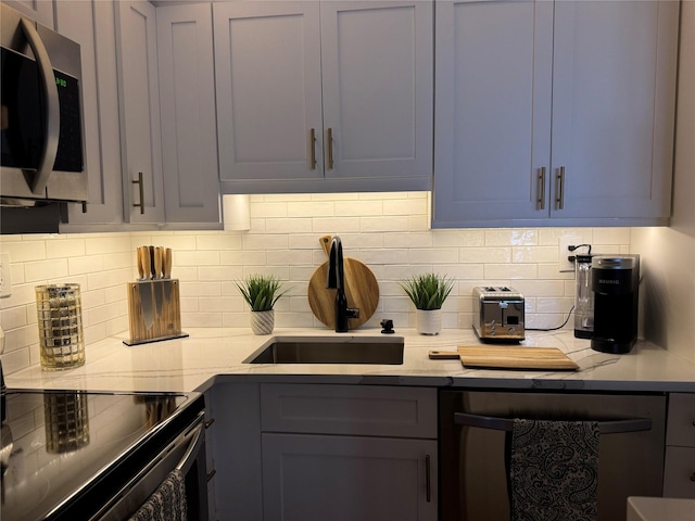 kitchen with stainless steel appliances, gray cabinets, sink, and decorative backsplash