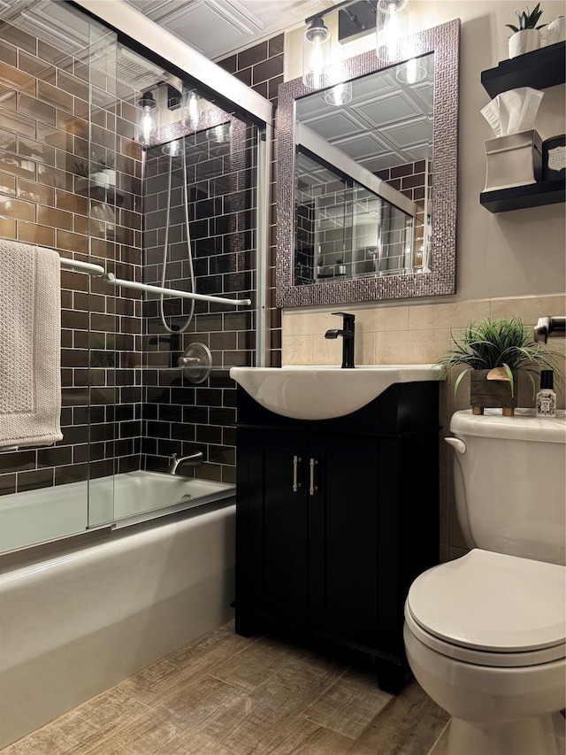 full bathroom with vanity, bath / shower combo with glass door, tile walls, and toilet