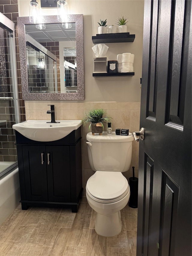 full bathroom featuring enclosed tub / shower combo, vanity, toilet, and tile walls