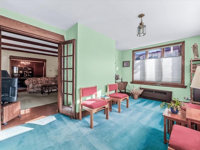 living area featuring radiator heating unit, a chandelier, beamed ceiling, and carpet