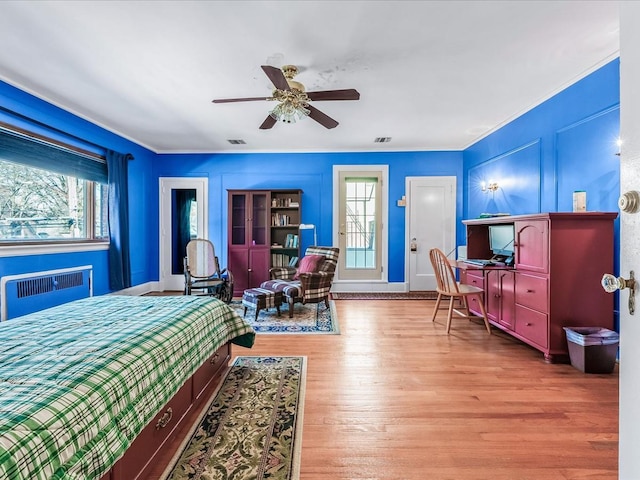 bedroom with ceiling fan, radiator heating unit, light hardwood / wood-style floors, and multiple windows