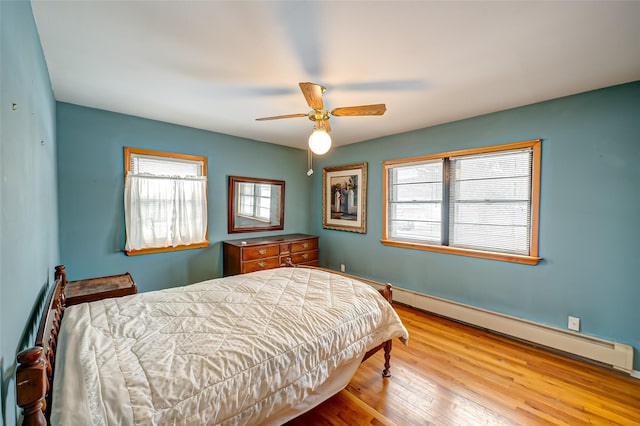 bedroom featuring ceiling fan, light hardwood / wood-style floors, multiple windows, and a baseboard heating unit